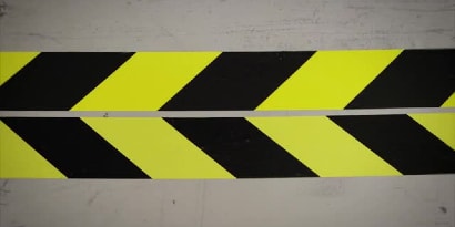 兩捲黑黃相間的膠帶並排放置的影片畫面，其相接的邊緣排列成指向左方的箭頭。
