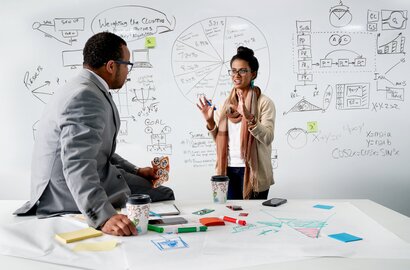 兩位專業人士在白板前討論商業策略，白板上有圖表與筆記。
