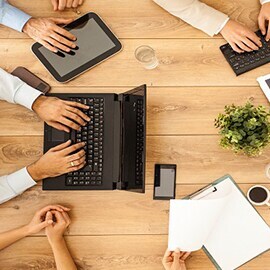 Close-up of people's hands resting on a wooden table using electronic devices