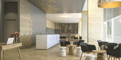 Lobby with comfortable chairs and tables, with walls that have graphic wraps and long desk with architectural finishes.
