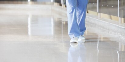 hospital employee in scrubs walking across a clean hallways floor.
