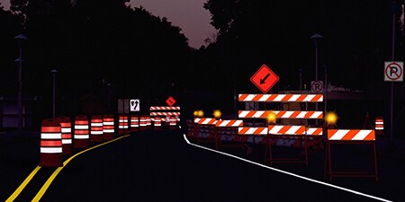 Temporary traffic control devices in a nighttime road work zone are illuminated by headlights.
