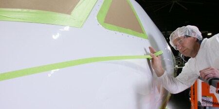 圖片顯示作業人員於駕駛艙窗戶已完成遮蔽的飛機機鼻貼覆遮蔽膠帶
