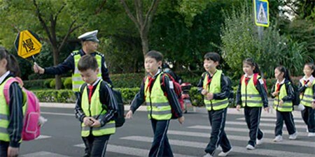 身穿安全背心的小學生與手持學區安全標誌的成人一起通過人行道。
