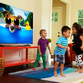 Small happy children dancing in front of a large flat screen television with a bright and colorful display screen.