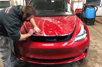 man applying 3M paint protection film to the hood of a black car