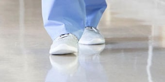 圖片顯示一名身穿一次性紙質長褲和鞋套的人，正沿著乾淨的地面朝鏡頭方向走來
