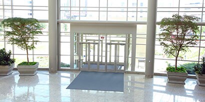 Interior shot looking outward of rotunda of a school facility with walls of glass and indoor trees on either side of the door.
