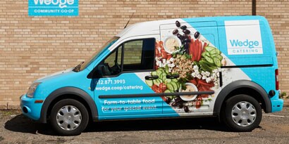 A delivery van’s vehicle wrap displays graphics and images to support its brand.
