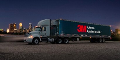 Semi-truck with blue vehicle wrap and reflective 3M logo, driving at night.
