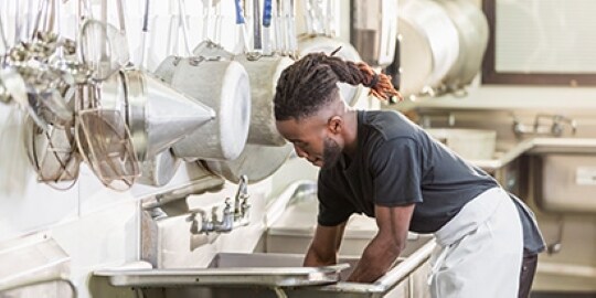 一名男子在商業廚房中清洗餐具
