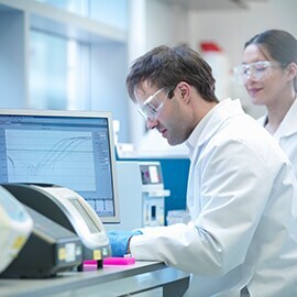 Scientists sitting at a desk behind a computer with safety glasses on