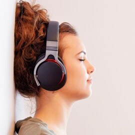 a woman leaning against a wall listening to music with wireless, over-the-ear headphones.