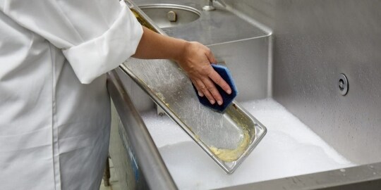 餐廳工作人員使用百利™ 蜂巢菜瓜布清潔附著焦痕的鍋具。
