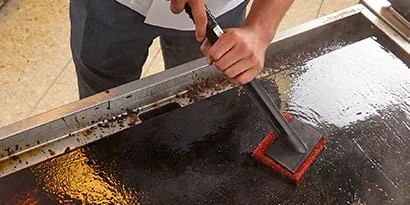 主廚使用清潔纖維與握把工具刷洗煎板
