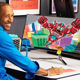 A smiling man in front of a large desktop monitor with a bright and colorful display screen.