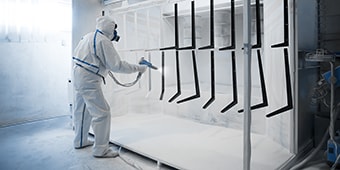 Image of a worker in protective gear applying powder coat paint to metal parts
