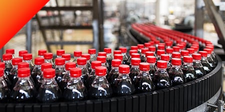 Hundreds of plastic bottles of dark soft drinks on a conveyer belt.
