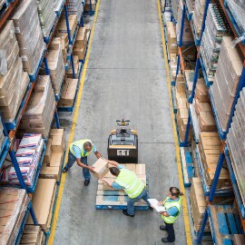 Overhead view of workers transferring cartons from a pallet to a shelf