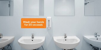 Orange wall graphic above the sinks in a public restroom reading “Wash your hands for 20 seconds.”
