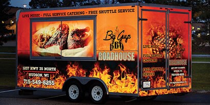Food truck trailer with orange and black fleet graphic featuring images of flames and grilled meat.