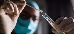 佩戴個人防護裝備的臨床醫生將測試拭子放入標有 COVID-19 的試管中。