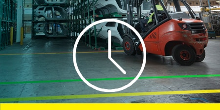 圖片顯示，堆高機正在將車架放到架子上，並行駛在以膠帶標示區域的地面上；畫面中疊加了一個時鐘圖示，象徵效率
