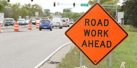 A highway work zone sign reads Road Work Ahead.
