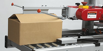 Image of a carton passing under the flap folding accessory and moving into the case sealer
