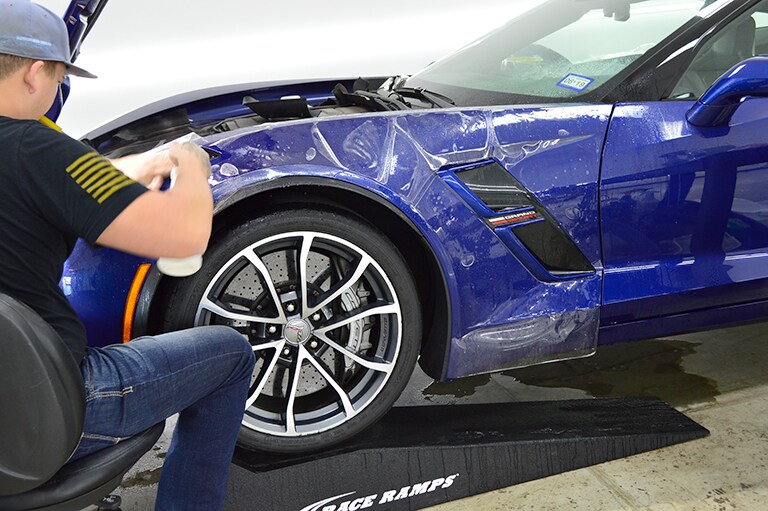 man applying 3M paint protection film on front left side of blue sports car
