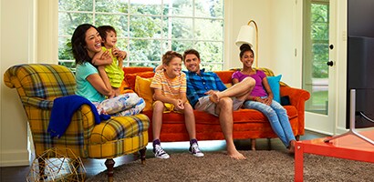 An image of a happy family in their living room looking at their flat screen television.
