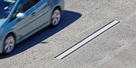 一輛藍色汽車飛速駛過人行道上清晰可見的高對比道路標記。
