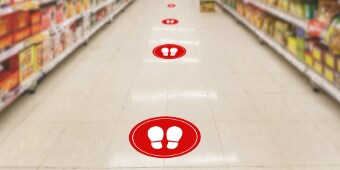 Floor graphics with white footprints in red circles showing recommended social distancing in a grocery store aisle.
