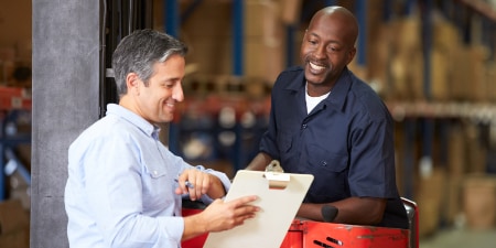 Image of a worker with clipboard consulting with a colleague operating a machine
