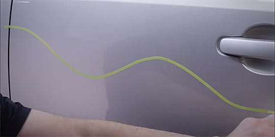 Text “Put pressure on the entire width of the crepe paper tape while stretching it” as a worker does this over a wheel well
