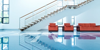 Lobby with clean, shiny floors, red chairs and couch, and long, modern staircase.
