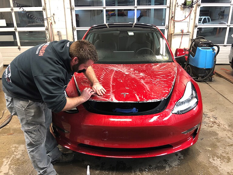 man applying 3M paint protection film to the hood of a black car
