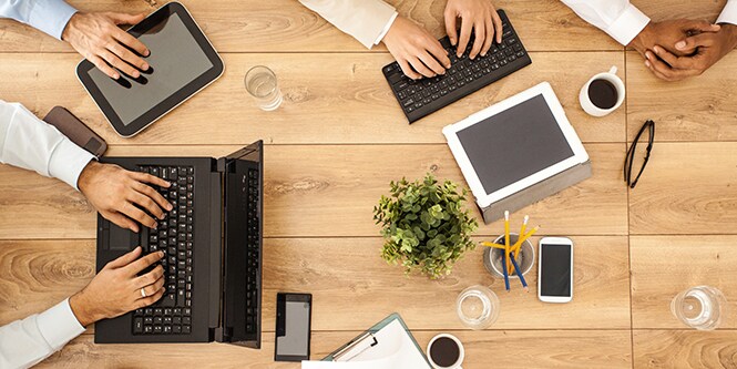 Overhead image of four people meeting at a table while looking at laptops and tablets 
