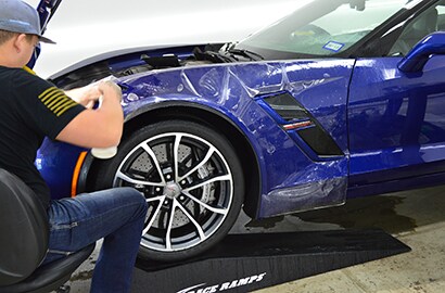 man applying 3M paint protection film on front left side of blue sports car