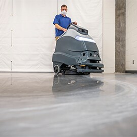 A worker operating a robotic floor scrubber to clean a commercial concrete floor.