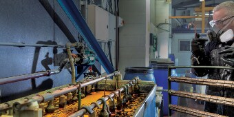 圖片顯示穿戴防護裝備的作業人員，準備將零件架掛入電鍍槽
