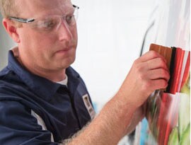 A graphic installer uses a squeegee to install a colorful vehicle wrap.