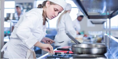 female chef adjusting the burner levels on a food service kitchen stove-stop.
