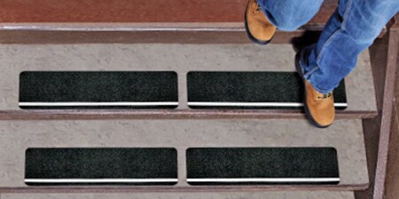 Person walking down a set of stairs with 3M anti-slip tapes and treads applied.
