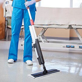 A nurse using a mop to clean the floor beside a hospital bed.