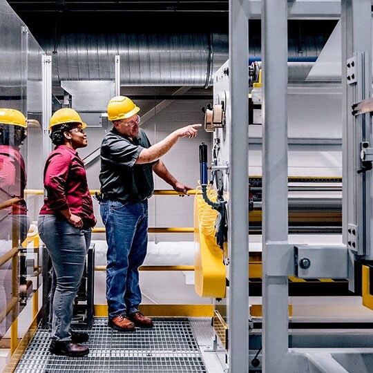 Image of two people in yellow hardhats examining items in facility