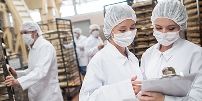 佩戴口罩和髮網的工作人員在商用廚房中討論
