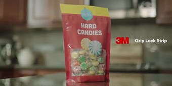 Video still of a resealable plastic pouch of hard candies and the words 3M™ Grip Lock Strip
