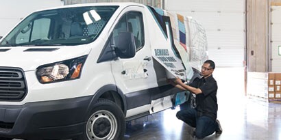 A graphic installer pulling a graphic wrap over a fleet vehicle